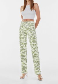 Gröna och vita zebra-randiga byxor med hög midja och rak ben-design, tillsammans med en åtsittande vit crop top och sandaler med klara klackar.