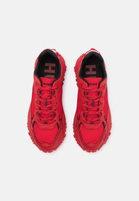 Paire de chaussures de sport rouges avec intérieur noir, lacets rouges et semelles texturées, vues de dessus sur fond blanc.