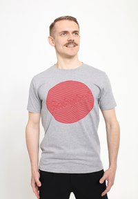 Graues Baumwoll-T-Shirt mit einem großen roten kreisförmigen Design, das strukturierte, gestreifte Effekte aufweist, und dem Wort "Babybel" in erhabenem Schriftzug.