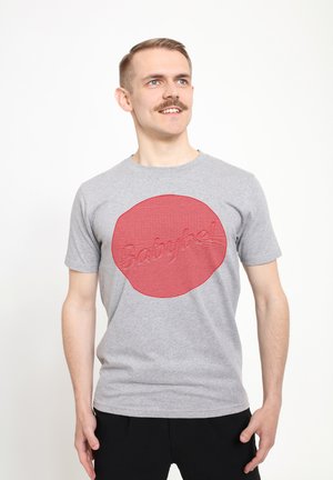 Graues Baumwoll-T-Shirt mit einem großen roten kreisförmigen Design, das strukturierte, gestreifte Effekte aufweist, und dem Wort "Babybel" in erhabenem Schriftzug.