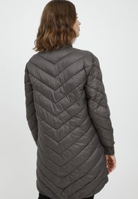 Pilkas paminkštintas paltas su chevrono raštu, turintis aukštą apykaklę ir mygtukus ant rankovių, pagamintas iš lengvo, tekstūruoto audinio.