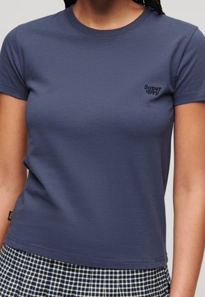 Kobieta nosząca dopasowany granatowy t-shirt Superdry w połączeniu z czarno-białą spódnicą w kratę.