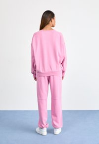 Roze sweatshirt en bijpassende broek van zachte stof, met een comfortabele pasvorm en geribbelde manchetten. Gekleed met witte sportschoenen.