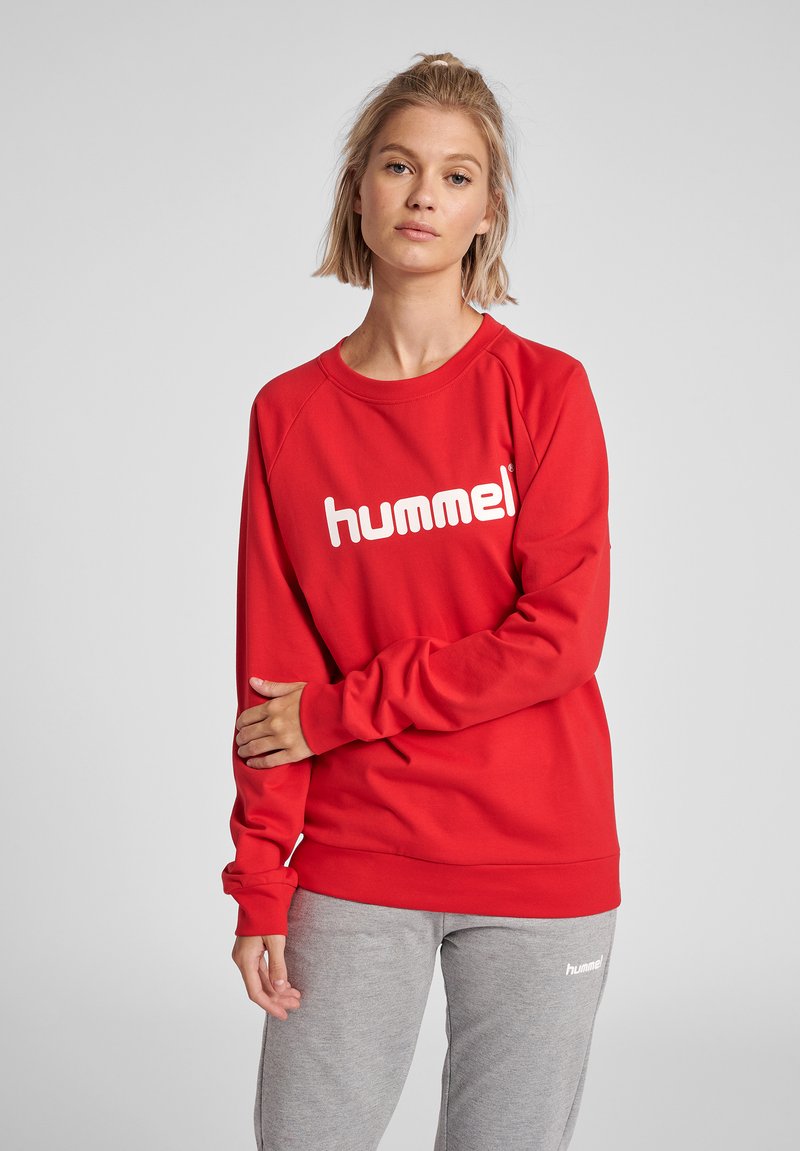 Felpa rossa con logo bianco "hummel", caratterizzata da un colletto rotondo e polsini a coste. Abbinata a pantaloni della tuta grigi, per un look informale.