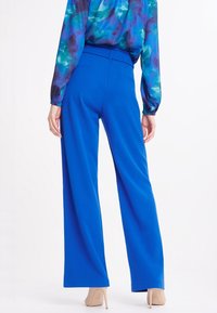 Pantalons larges bleu royal à taille haute, en tissu lisse, avec des plis subtils et un look épuré et taillé.