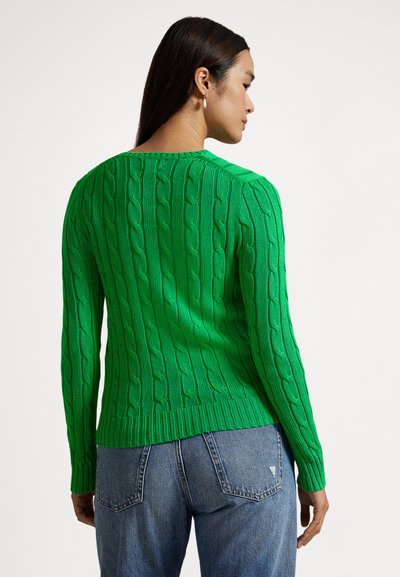 Grønn strikket genser med teksturert kabelmønster, lange ermer og ribbet kant. Kombinert med blå jeans.