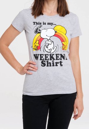 Vrouw draagt een grijs T-shirt met Snoopy en Woodstock dansend onder een regenboog en de tekst "Dit is mijn weekendshirt."