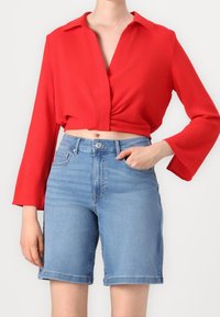 Czerwona krótką bluzkę z kołnierzykiem i długimi rękawami, w zestawieniu z jasnoniebieskimi szortami dżinsowymi z klasycznym pięciokomorowym wzorem.