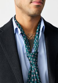 Silk tie in dark green with a floral pattern featuring red and white accents; displayed with a light blue shirt and black jacket.