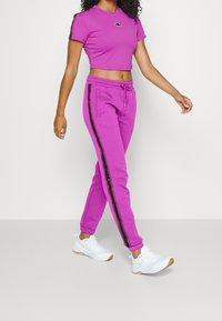 Bright pink cropped t-shirt with a small logo, paired with matching pink sweatpants featuring black side stripes and ankle cuffs. White sneakers.