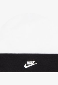 Căciulă tip beanie alb-negru cu textură tricotată moale; are o parte superioară albă, o bandă neagră și un logo Nike brodat pe față.