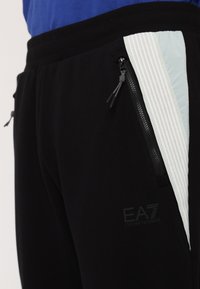 Sorte joggers med en struktureret lys blå detalje, med lynlåslommer og et EA7-logo, lavet af blødt, åndbart materiale.