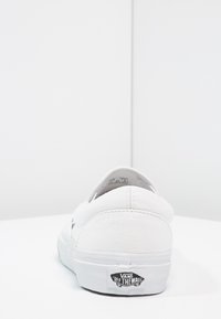 Baskets en toile blanches avec une tige texturée, profil bas et logo noir "Vans Off the Wall" au dos. Design simple et épuré.