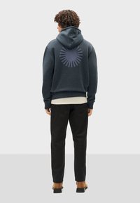 Donkerblauwe hoodie met een ronde graphic op de achterkant, textuurstof en een relaxte pasvorm. Gecombineerd met zwarte broek en casual schoeisel.