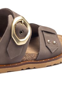Graue Wildleder-Sandale mit einer großen goldenen achteckigen Schnalle, Korkfußbett und strukturiertem Laufsohle, die dekorative Nähte und metallische Akzente aufweist.