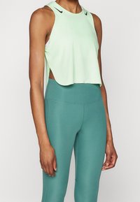 Lichtgroene mouwloze cropped top met een afgeronde zoom en zijopeningen, gecombineerd met teal hooggetailleerde leggings met een gladde textuur.