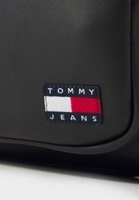 Black synthetic material with a textured finish; features a rectangular embroidered patch with "TOMMY JEANS" and red, white, and blue accents.