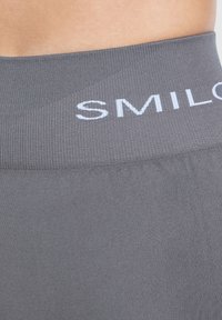Grijze sportlegging met een ribbelige tailleband en witte "SMIL" tekst. De stof is glad met een lichte glans en rek.