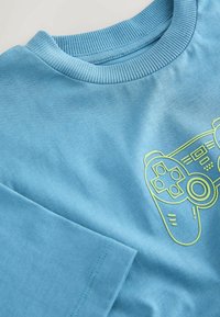 Light blue cotton t-shirt with a ribbed crew neck and short sleeves, featuring a yellow graphic of a gaming controller on the front.