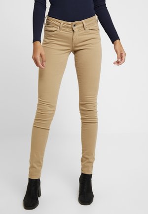 Beżowe obcisłe spodnie z mieszanki bawełny, z pięcioma kieszeniami, szlufkami na pasek i srebrnymi elementami. Noszone z czarnymi botkami na obcasie.