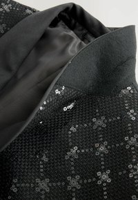 Fekete, texturált anyag, virágmintás flitterekkel. Simább belső bélés, széles gallér és letisztult dizájn.