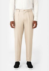 Beige veckade byxor med avslappnad passform, med knappstängning och sidofickor. Matchat med svarta sneakers för en avslappnad look.