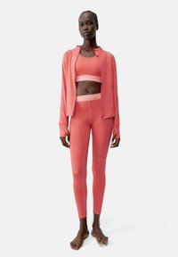 Koral sportset som inkluderar en kortärmad topp och högmidjade leggings med en mjuk, elastisk textur; en zip-up jacka fulländar looken.