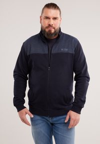 Mornarska majica sa zipom, kontrastnim tamnoplavo-škim panelima na ramenima, rebrastim manžetama i donjem rubu, logom na prsima i bočnim džepovima. Udobna tkanina.