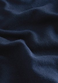 Nāvijas zilas adītas auduma ar gludu tekstūru, kurā ir redzamas smalkas krāsu un locījumu variācijas, kas norāda uz mīkstu un elastīgu sastāvu.