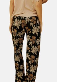 Pantalons noirs avec un motif floral coloré comprenant de grandes feuilles ivoire et de petits accents rouges. Le tissu semble doux avec une coupe décontractée.