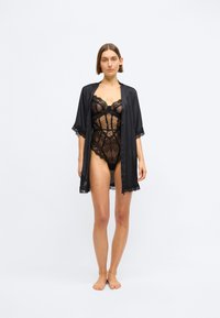 Črno prosojno čipkasto bodi s pikicami, obrobljenimi skodelicami, v kombinaciji z enobarvnim črnim satenskim kimonom z čipkastim obrobom na rokavih.