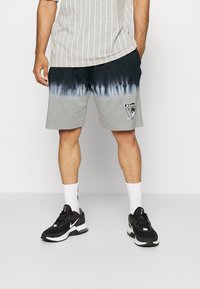 Shorts tie-dye grigi e neri con cinturino elastico, con il logo dei Raiders sulla gamba sinistra. Abbinati a sneaker nere e calze bianche.