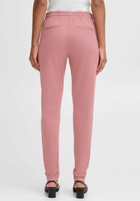 Stretchy, pink fabric trousers with a slim fit, elastic waistband, and two back pockets. Smooth texture, no visible patterns or embellishments.