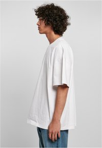 T-shirt bianco in cotone con maniche corte, vestibilità rilassata, collo tondo e una leggera texture; abbinato a jeans in denim blu.