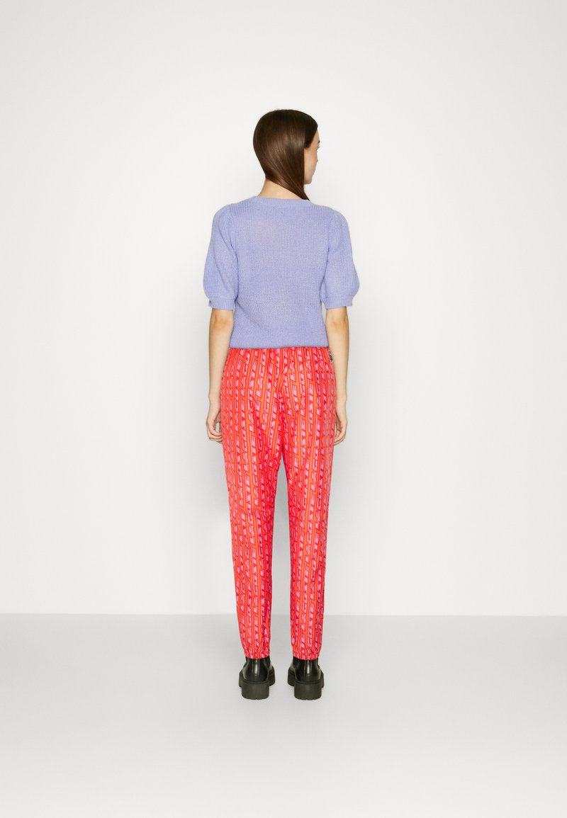 Suéter de punto morado claro con mangas abullonadas combinado con pantalones rojos de patrón que presentan diseños verticales. Zapatos de plataforma negros visibles.