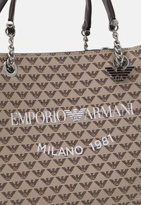 Bordowa skórzana torebka z wytłoczonym wzorem logo, srebrnymi akcentami i dwoma paskami na ramię. Posiada białą nazwę marki i datę.