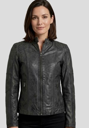Woman with shoulder-length brown hair wearing a zipped dark gray leather jacket with zippered side pockets, standing against a plain background.