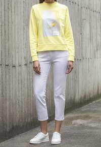 Sudadera amarilla con un gráfico floral, combinada con pantalones cortos blancos y zapatillas blancas. Tela suave y corte relajado.