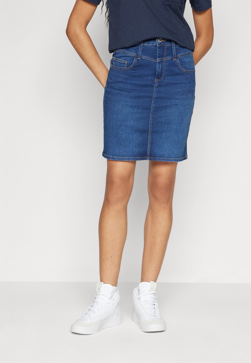 Denim skirt in medium blue, knee-length, with a straight cut, five-pocket design, and subtle stitching details; paired with white sneakers.