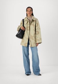 Lys beige kåpe med stort blomstermønster, løs passform og trykknapper, brukt over en beige høyhalset genser og parret med blå vide jeans.