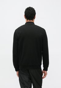 Μαύρο φούτερ με στρογγυλή λαιμόκοψη, ριμπ μανσέτες και τελείωμα. Κατασκευασμένο από απαλό ύφασμα, διαθέτει καθαρό πίσω μέρος χωρίς ορατά λογότυπα.