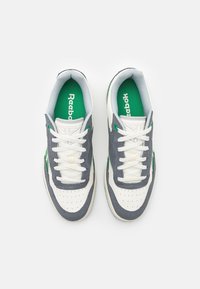 Vita och grå sneakers i mocka och lädermaterial, med gröna detaljer, perforerad tå och vita snören. Reebok-logotyp på innersulorna.