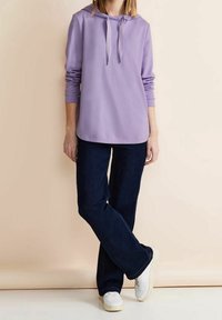 Ljuslila hoodie med dragsko, långa ärmar och rundad nederkant, kombinerad med mörkblå utsvängda jeans och vita sneakers.