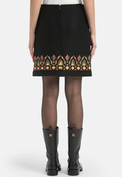 Crna suknja s šarenim geometrijskim vezom na rubu. Ima zatvarač na leđima i kombinira se s crnim kožnim čizmama.