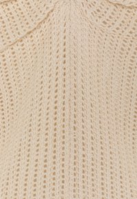 Pull en tricot crème avec un motif texturé, trame ouverte et col rabattu. Matériau doux avec des détails de couture verticaux.