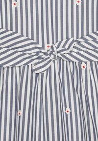 Gestreiftes Kleid in Blau und Weiß mit einem geknoteten Taillendetail. Besitzt rot-weiße bestickte Blumen auf dem Stoff.