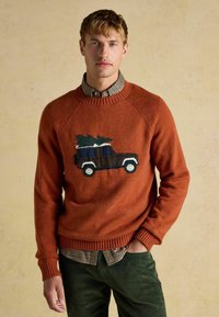 Raundivärviline kudumispusakas, mille esiosas on sõiduki ja puu muster. Sellel on soonikkoes kaelus ja mansetid. Kandmine ruudulise särgi peal.