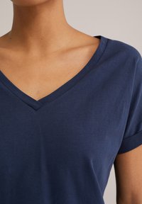 Navy zilgans kokvilnas t-krekls ar V veida kakla izgriezumu un īsām rullētām piedurknēm, kas izceļas ar gludu tekstūru un vienkrāsainu bez rakstiem vai akcentiem.