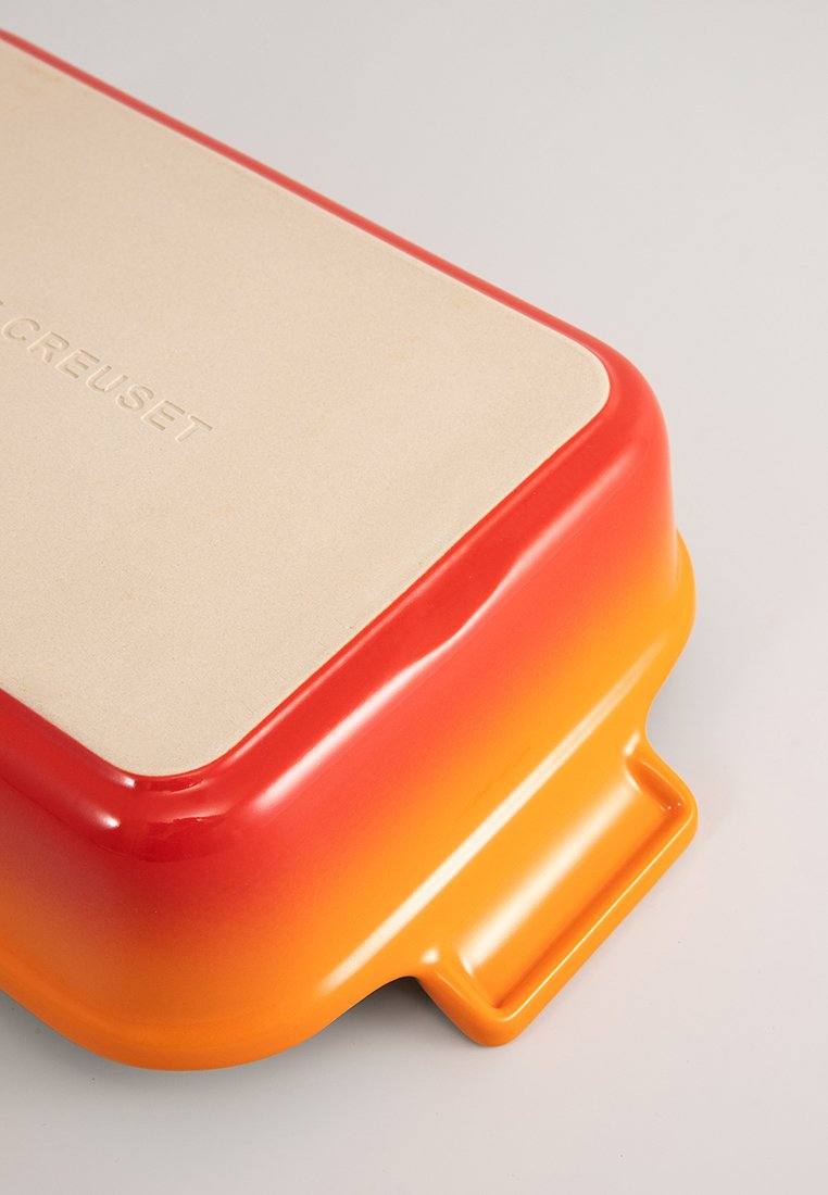 Rechteckiges keramisches Kochgeschirr in Orange- und Rotgradient mit einem beigen, strukturierten Deckel, der mit "Le Creuset" geprägt ist.