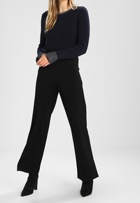 Námořnický pletený svetr s dlouhým rukávem, se šedým akcentem na výstřihu, spárovaný s černými širokými nohavicemi a černými lodičkami.